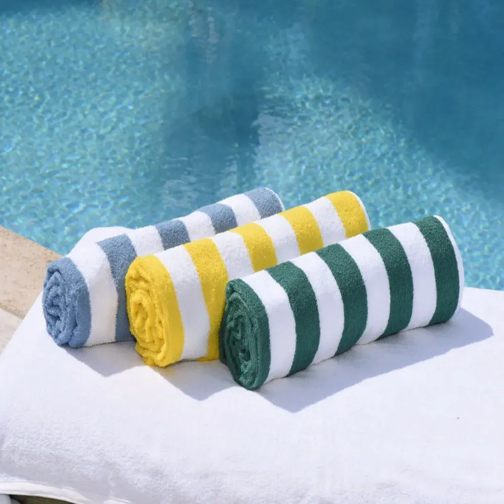 Drei gerollte Pooltücher mit Blockstreifen in Blau, Gelb und Grün neben einem Schwimmbecken