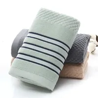 Asciugamano viso color menta con righe tessute blu navy; sullo sfondo, asciugamani grigi e beige