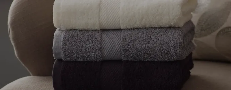 Close view of three stacked terry towels in ivory, grey and charcoal with honeycomb borders