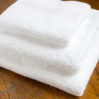 Tres toallas de baño blancas y gruesas dobladas sobre una mesa de madera