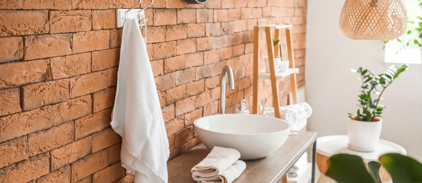 Weißes Frottierhandtuch hängt neben einem Waschbecken in einem Badezimmer mit Ziegelwand