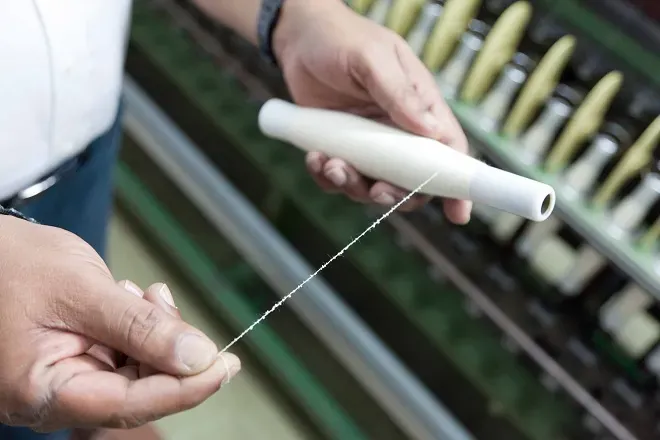 Hands checking yarn drawn from a cone